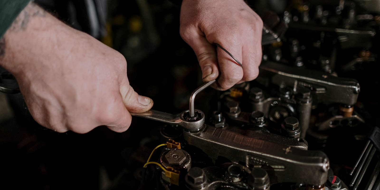 Licensed stock photograph: two hands working a wrench and a hex key on the top of an engine.