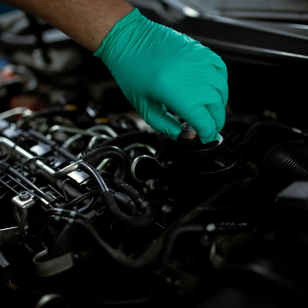 Licensed stock photograph: a gloved hand lifting the oil filler cap on an engine.