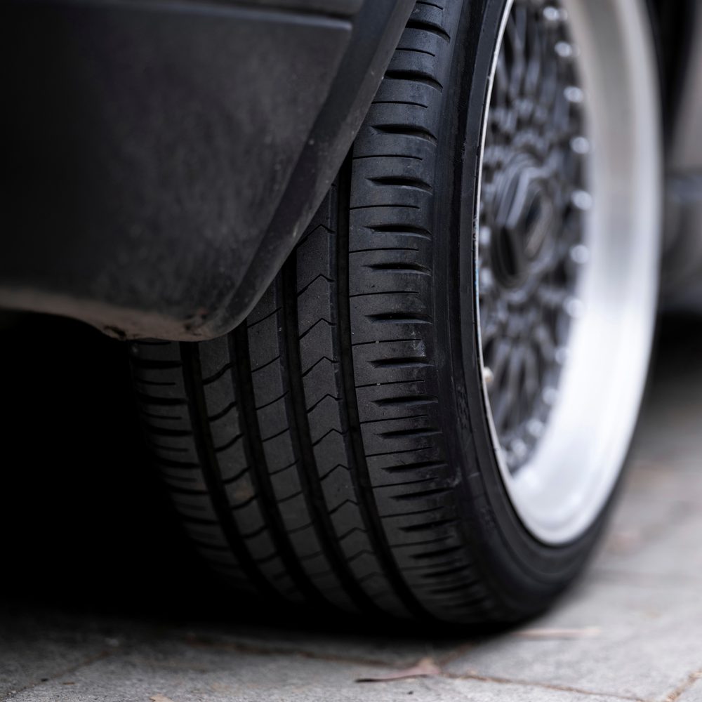 Licensed stock photograph: the tread of a car tire and the edge of its wheel, low to the ground.